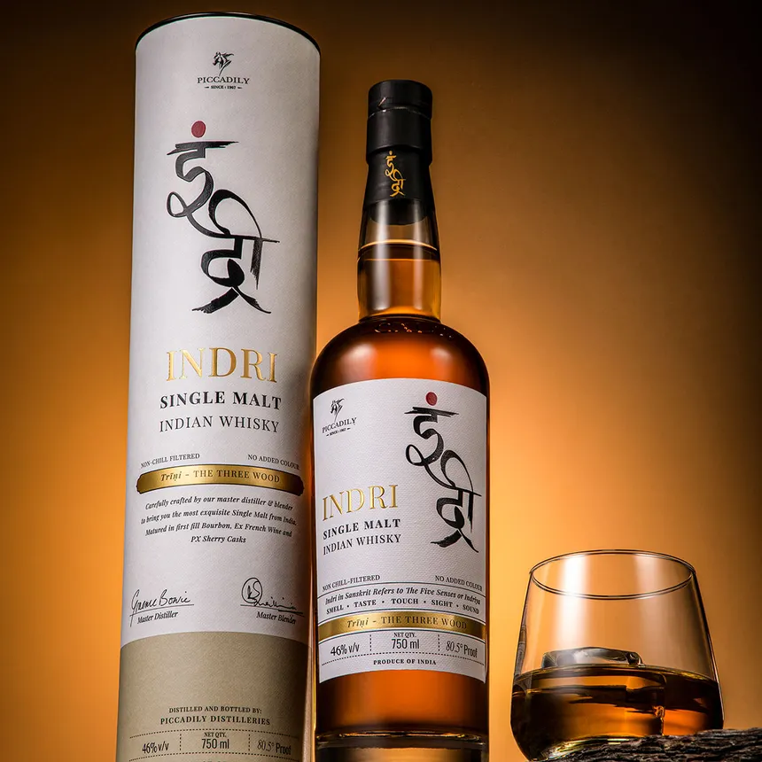 Indri Trini single malt bottle with its tube and a poured glass, amber studio light